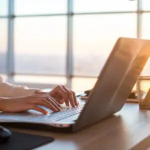 Hands typing on laptop at sunlit desk